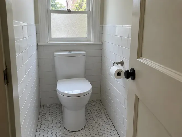 Clean white toilet in a small tiled bathroom with a frosted window in Petersham