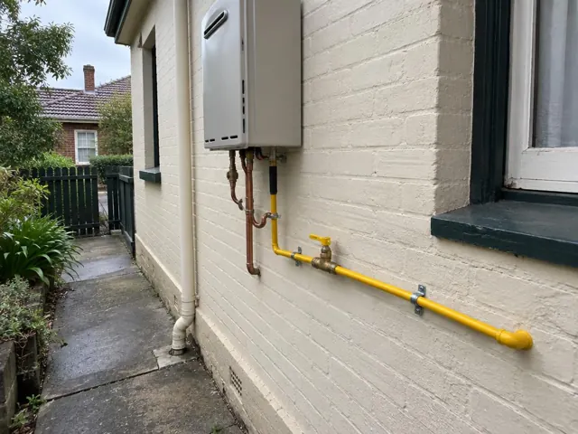 Yellow gas pipe and wall-mounted meter on a cream brick exterior wall beside a window in Petersham
